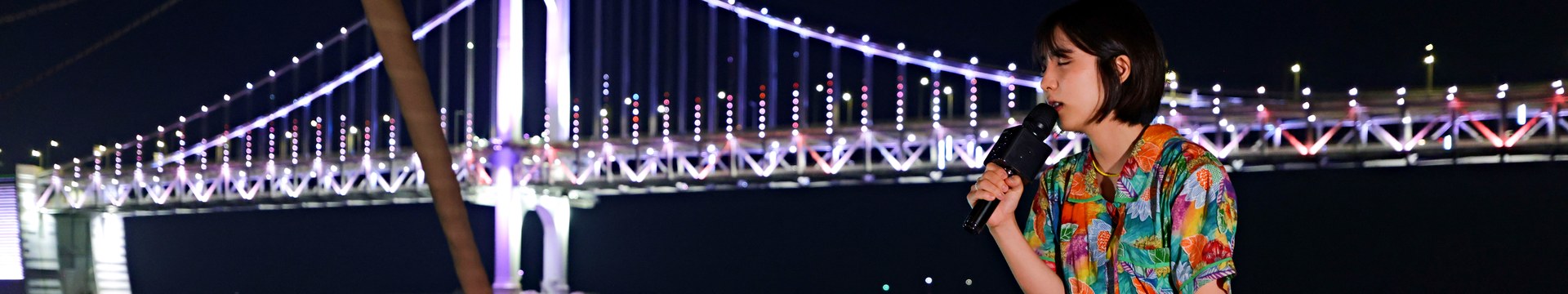 광안대교를 배경으로 요트 뱃머리에서 노래하는 버스킹 공연자